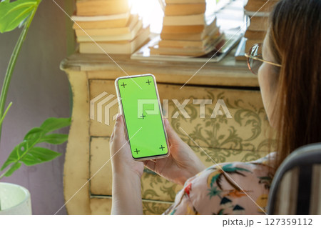 cell phone blank green screen mockup. woman holding mobile phone in hand, using smartphone at living room for work contact or entertainment. room decorate with vintage cabinet, book, Monstera tree cell phone blank green screen mockup. woman holding mobile phone in hand, using smartphone at living room for work contact or entertainment. room decorate with vintage cabinet, book, Monstera tree 127359112