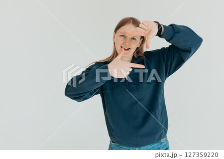 Young positive woman makes camera frame with fingers tilts head and smiles happily searches perfect angle has playful mood 127359220