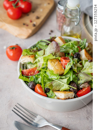 Vegetable salad with lettuce, tomatoes, croutons and olives in a bowl on a light background 127359254