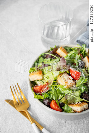 Salad with lettuce, tomatoes, croutons, olives and parmesan cheese in a bowl on a light background Salad with lettuce, tomatoes, croutons, olives and parmesan cheese in a bowl on a light background 127359256
