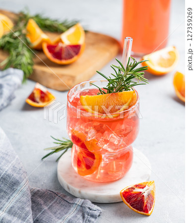 Blood orange cocktail with ice and rosemary on a light background with citrus fruits and napkin. Blood orange cocktail with ice and rosemary on a light background with citrus fruits and napkin. 127359269