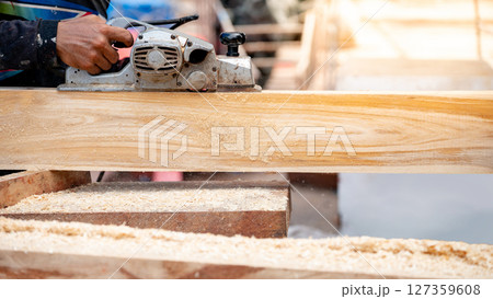 Male carpenter hand using an electric planer on wooden plank in workshop 127359608