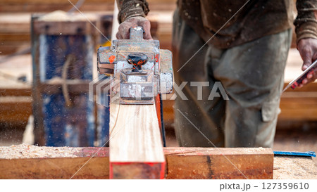 Male carpenter hand using an electric planer on wooden plank in workshop 127359610