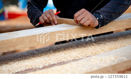 Male carpenter hand placing a piece of wood and use pencil to draw a line for cutting wooden plank 127359611