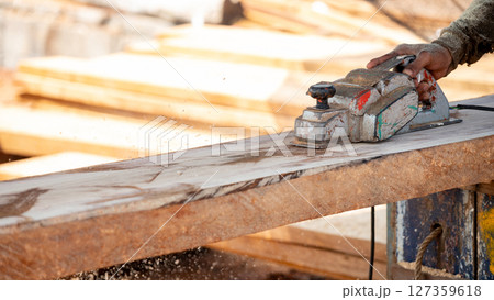 Male carpenter hand using an electric planer on wooden plank in workshop Male carpenter hand using an electric planer on wooden plank in workshop 127359618