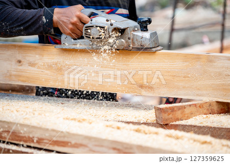 Male carpenter hand using an electric planer on wooden plank in workshop Male carpenter hand using an electric planer on wooden plank in workshop 127359625