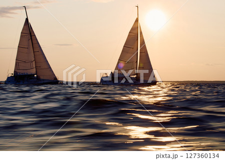 Two sailboats are moving at high speed at sunset, sailing regatta in the Gulf of Finland at sunset, sailing yacht competing in a race, splashing water from under the boat, teamwork, board the boat Two sailboats are moving at high speed at sunset, sailing regatta in the Gulf of Finland at sunset, sailing yacht competing in a race, splashing water from under the boat, teamwork, board the boat 127360134