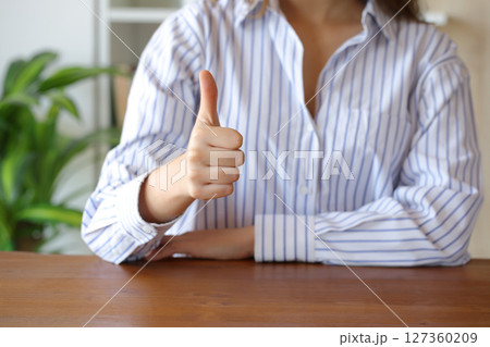Woman gesturing thumbs up at home on a table Woman gesturing thumbs up at home on a table 127360209