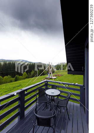 Scenic View from a Cozy Balcony Overlooking Lush Green Fields and Darkening Clouds, Perfect for a Relaxing Getaway in Nature's Embrace Amidst the Mountains 127360239