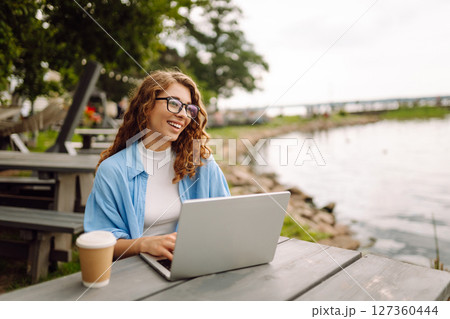 Beautiful female freelancer working online using laptop enjoying natural landscape overlooking lake. 127360444