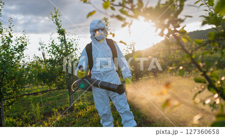 Farmer spraying pesticide in orchard, disinfecting trees in protective suit. Farmer spraying pesticide in orchard, disinfecting trees in protective suit. 127360658