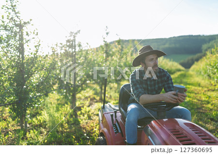 Farmer sitting on small tractor in orchard, enjoying peaceful moment. Farmer sitting on small tractor in orchard, enjoying peaceful moment. 127360695