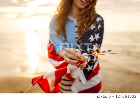 Young woman with American flag and sparklers on beach. Patriotic holiday. USA celebrate 4th of July. Young woman with American flag and sparklers on beach. Patriotic holiday. USA celebrate 4th of July. 127361832