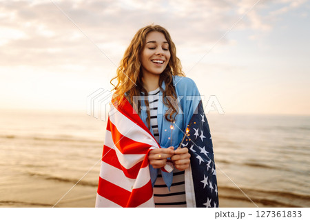Young woman with American flag and sparklers on beach. Patriotic holiday. USA celebrate 4th of July. Young woman with American flag and sparklers on beach. Patriotic holiday. USA celebrate 4th of July. 127361833