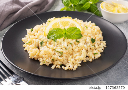 Boiled bulgur with fresh lemon and mint on a plate. A traditional oriental dish called Tabouleh. Gray concrete background Boiled bulgur with fresh lemon and mint on a plate. A traditional oriental dish called Tabouleh. Gray concrete background 127362270