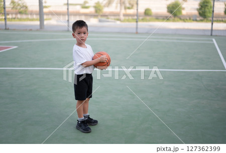 Focused boy holding basketball on court ready for play. Focused boy holding basketball on court ready for play. 127362399