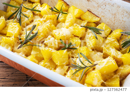 Delicious baked potatoes with spices cheese and rosemary in a ceramic baking tray on a wooden rustic background. Close up 127362477