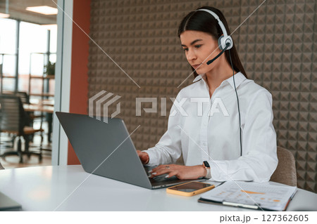 Beautiful young woman is sitting by laptop in the office Beautiful young woman is sitting by laptop in the office 127362605