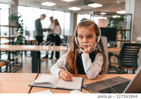 Laptop is on the table. Little girl is in the office where people working together Laptop is on the table. Little girl is in the office where people working together 127363864