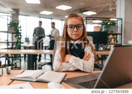 Laptop is on the table. Little girl is in the office where people working together Laptop is on the table. Little girl is in the office where people working together 127363866