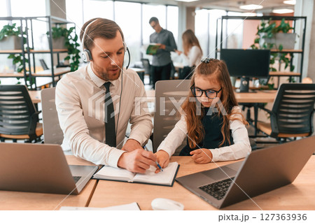 Man is helping, teaching. Little girl is in the office where people working together 127363936
