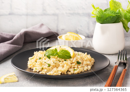 Boiled bulgur with fresh lemon and mint on a plate. A traditional oriental dish called Tabouleh. Gray concrete background Boiled bulgur with fresh lemon and mint on a plate. A traditional oriental dish called Tabouleh. Gray concrete background 127364365