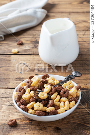 Dry breakfast cereals. Chocolate and corn rings made from natural cereals with milk in a plate. Wooden rustic background, copy space. 127364404