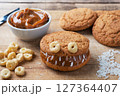 Cookies with cream paste in the shape of monsters for Halloween celebration. Funny homemade faces made of oatmeal cookies and boiled condensed milk. 127364407