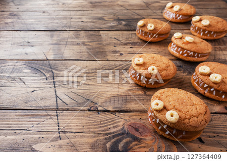 Cookies with cream paste in the shape of monsters for Halloween celebration. Funny homemade faces made of oatmeal cookies and boiled condensed milk. copy space 127364409