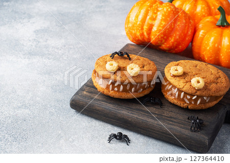 Cookies with cream paste in the shape of monsters for Halloween celebration. Funny homemade faces made of oatmeal cookies and boiled condensed milk. copy space 127364410