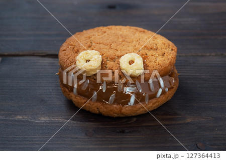 Cookies with cream paste in the shape of monsters for Halloween celebration. Funny homemade faces made of oatmeal cookies and boiled condensed milk. copy space 127364413