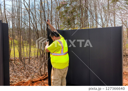 Worker secures black panels for shed in wooded location, showcasing construction activity under assembling storage 127366640