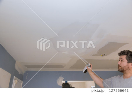 Contractor is applying spray paint to ceiling of room with blue walls already painted in during for renovation. 127366641