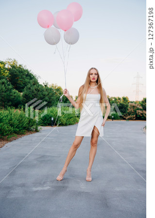 Beautiful slender blonde with long hair and balloons in an evening park. 127367198