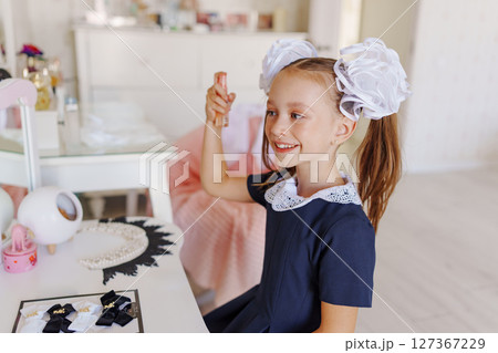 A little girl in a school uniform preens herself at a dressing table. A little girl in a school uniform preens herself at a dressing table. 127367229