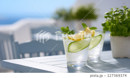 Two spa spritz cocktails with cucumber and lemon sit on a white table under a clear blue sky 127369374
