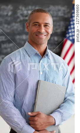 Teacher holds a book and stands proudly in front of students with the USA flag on Labor Day Teacher holds a book and stands proudly in front of students with the USA flag on Labor Day 127369660