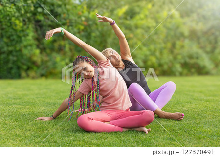 Girl and mature woman are practicing gymnastic  together sitting at the garden. 127370491