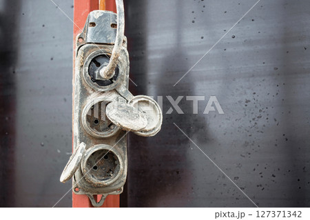 Electrical outlet attached to a wall in a rustic setting showing signs of wear and weathering 127371342