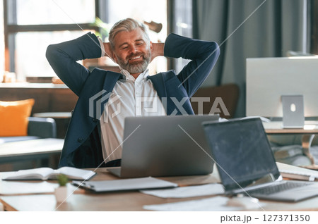 Taking a break, satisfied with success. Senior businessman is working in the office Taking a break, satisfied with success. Senior businessman is working in the office 127371350