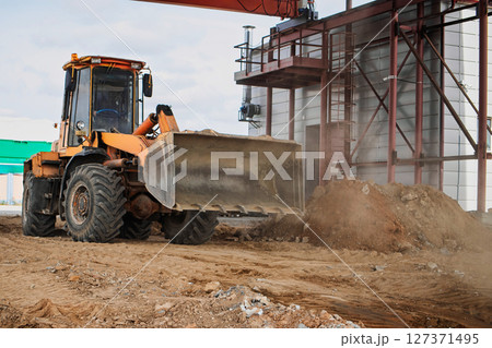 Construction site activity with a heavy machinery loader moving dirt near a building 127371495