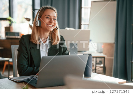 Smiling, using laptop. Young beautiful woman in formal clothes is working in the office 127371545