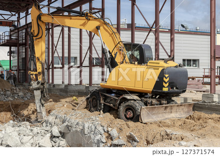 Professional demolition of reinforced concrete structures using industrial hydraulic hammer with excavator. Rods of metal fittings. Wreckage and crumbles of concrete. 127371574