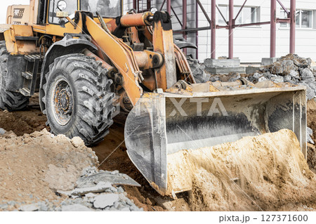 A powerful front loader on the construction site performs sanding. Moving soil with construction equipment. Excavation. A powerful front loader on the construction site performs sanding. Moving soil with construction equipment. Excavation. 127371600