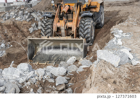 A front-end loader at a construction site removes debris from reinforced concrete. Collection and removal of detached building materials. 127371603