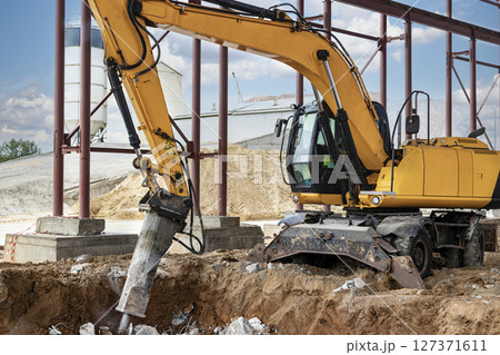 Professional demolition of reinforced concrete structures using industrial hydraulic hammer with excavator. Rods of metal fittings. Wreckage and crumbles of concrete. Professional demolition of reinforced concrete structures using industrial hydraulic hammer with excavator. Rods of metal fittings. Wreckage and crumbles of concrete. 127371611