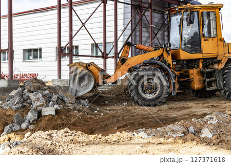 A front-end loader at a construction site removes debris from reinforced concrete. Collection and removal of detached building materials. 127371618