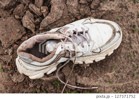 Old worn-out sneaker rests on dry, cracked earth with scattered dirt and rocks in a natural landscape 127371752