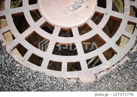 Rusty drain cover resting on asphalt during daylight in an urban environment Rusty drain cover resting on asphalt during daylight in an urban environment 127371776
