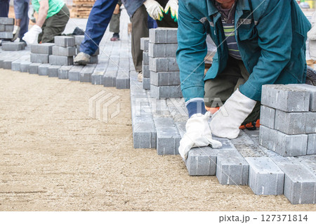 Workers laying gray bricks on a construction site in daytime for pathway installation Workers laying gray bricks on a construction site in daytime for pathway installation 127371814